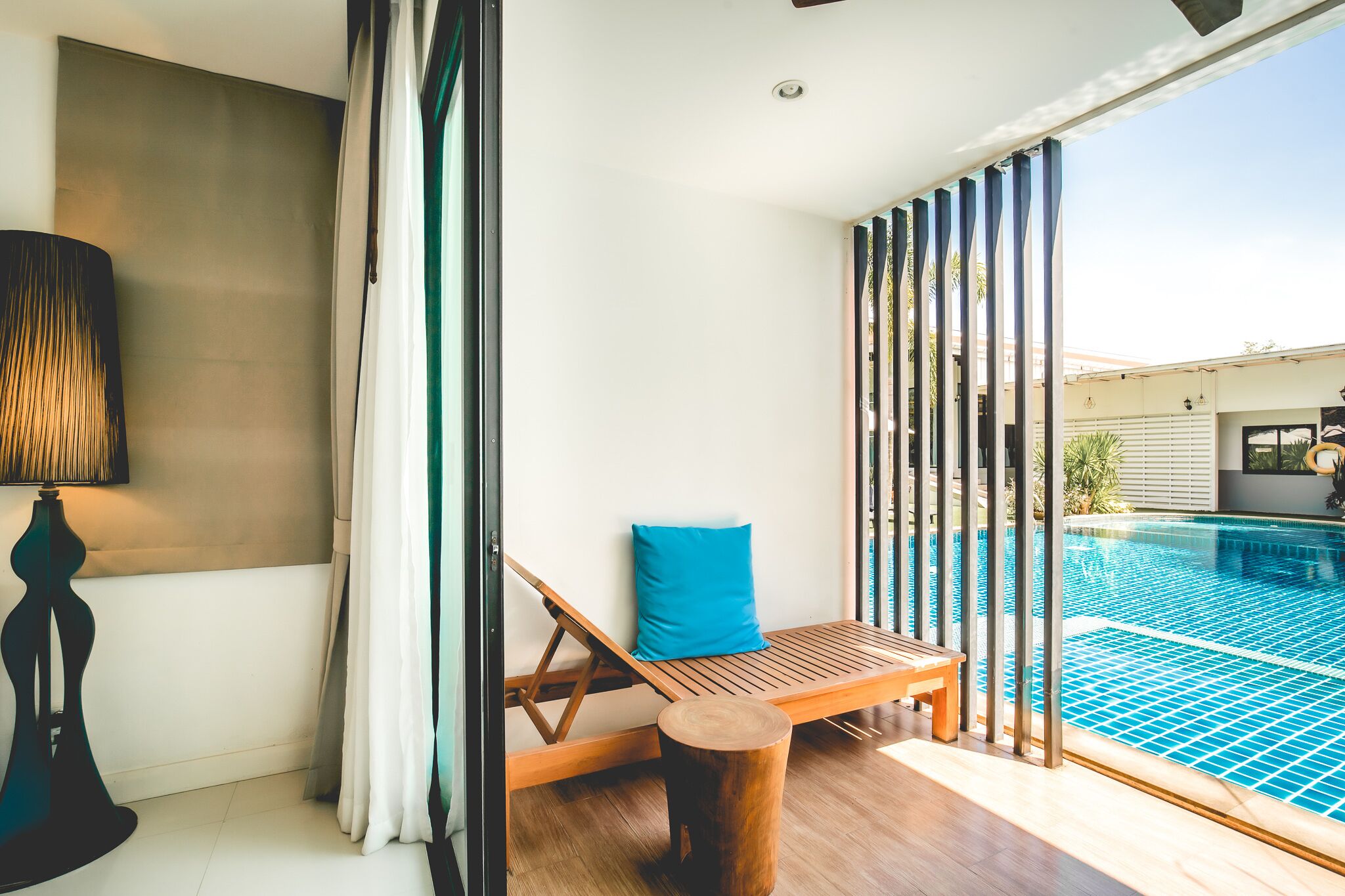Un área junto a la piscina con una silla de madera, un cojín azul y un taburete de madera.