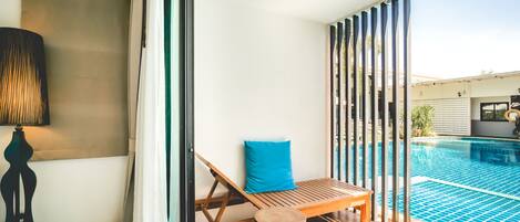 Un área junto a la piscina con una silla de madera, un cojín azul y un taburete de madera.