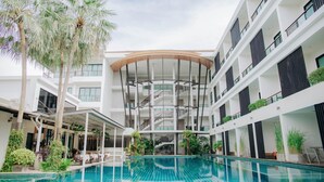 Un hotel moderno con piscina central, varios balcones y plantas de interior.