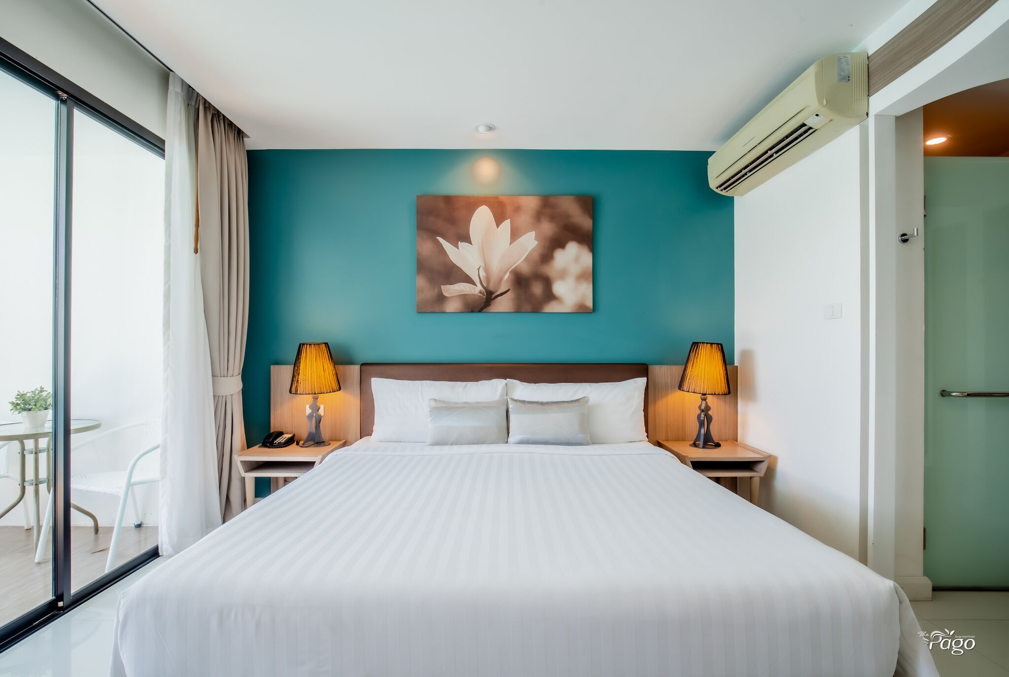 A hotel room with a large bed, two bedside tables with lamps, a wall-mounted air conditioner, and a window with curtains.