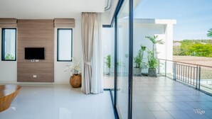 Una sala de estar moderna con una televisión de pantalla plana, una pared de acento de madera, un ventanal con cortinas y un balcón con plantas en macetas.