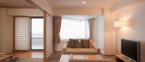 Una habitación de hotel moderna con sofá, televisión, lámpara y puerta corredera que da a un balcón.