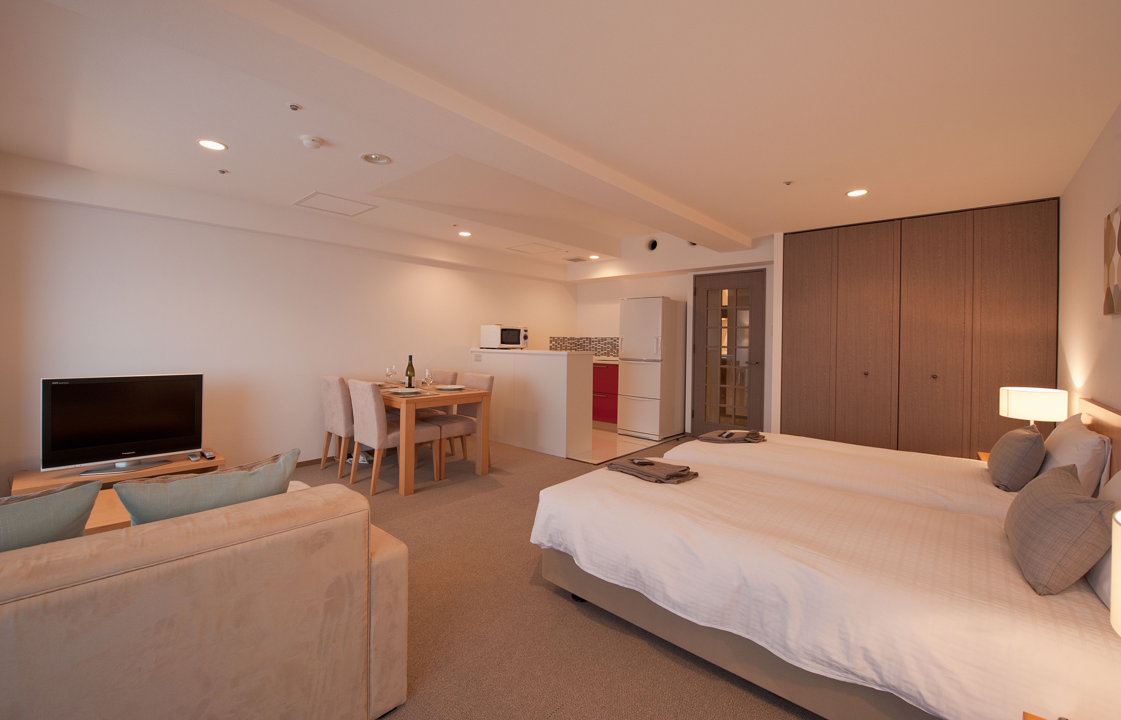Habitación de hotel con cama, televisor, sofá, escritorio con silla y kitchenette.