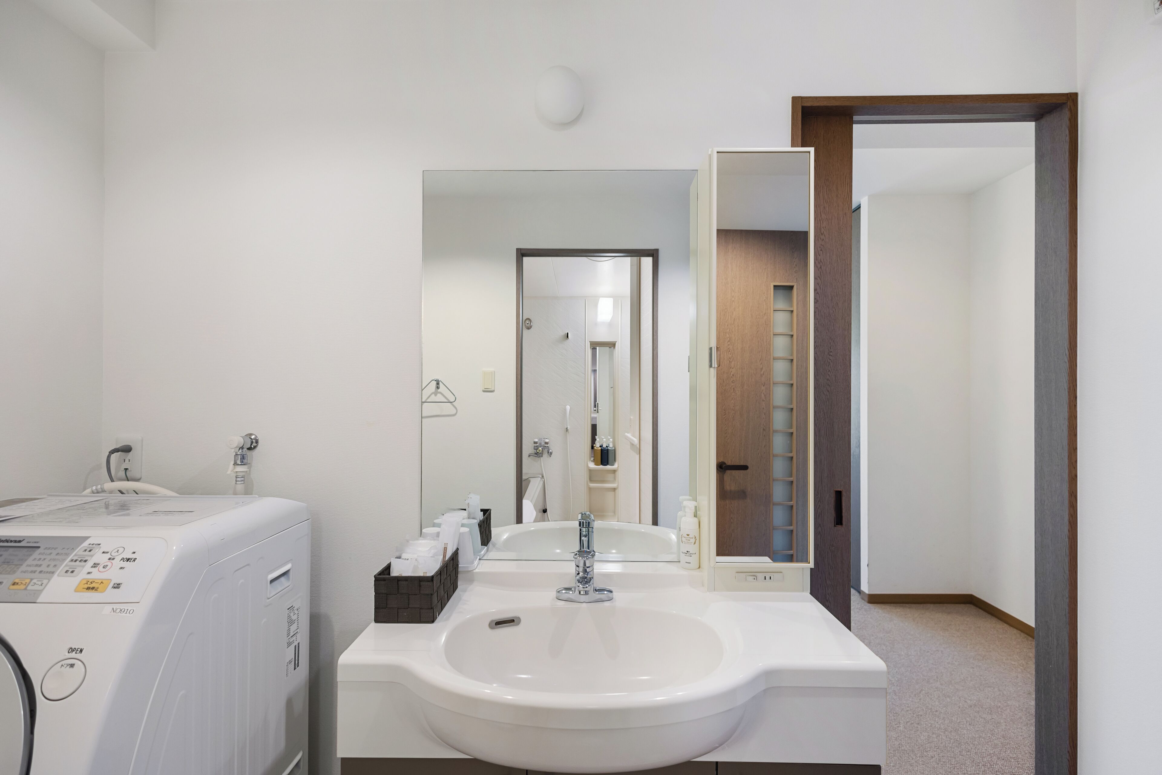 A modern bathroom with a white sink, a mirror, and a washing machine.