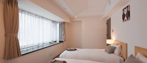 A hotel room with two beds, a window with curtains, a wall-mounted lamp, and a painting.
