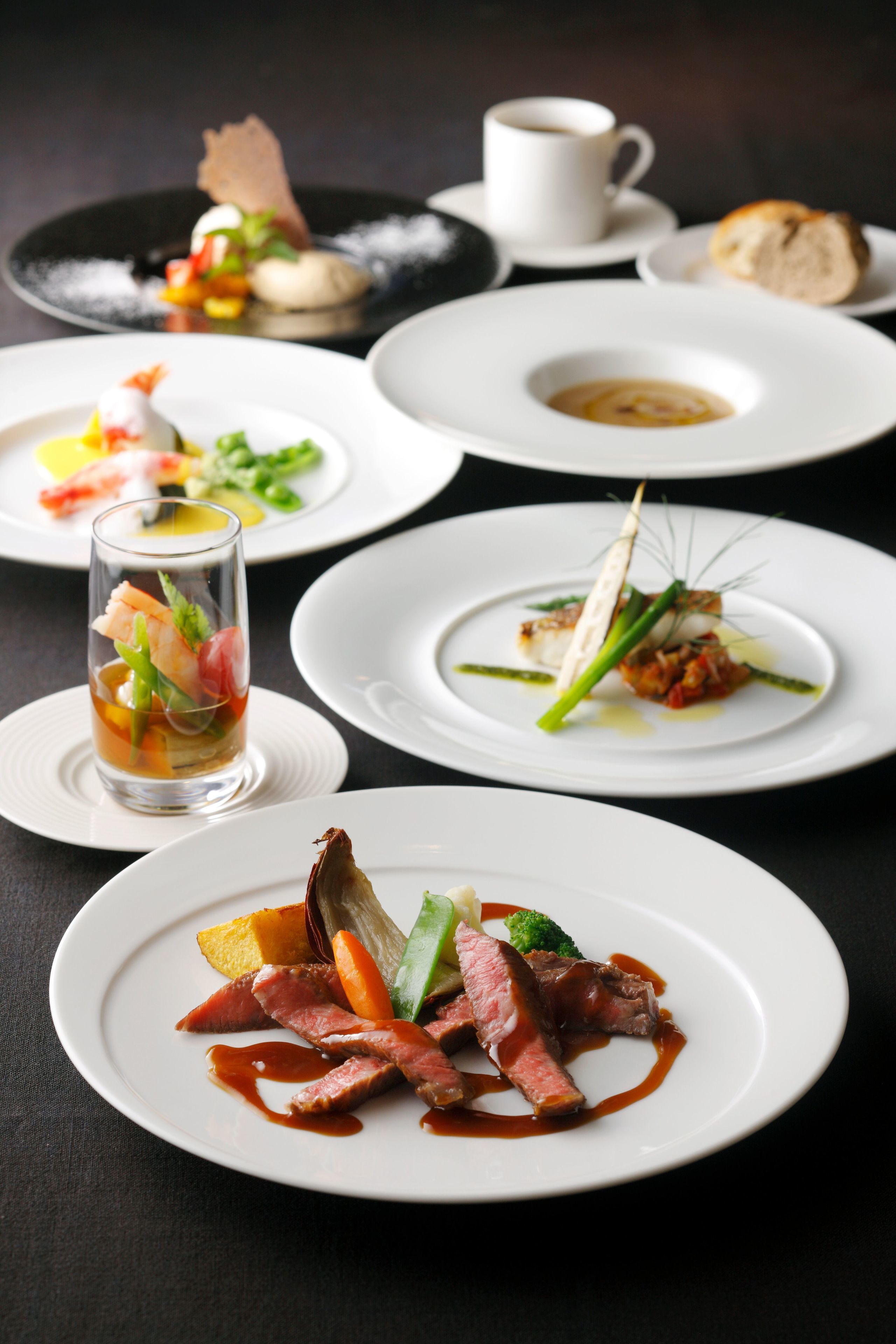 A variety of dishes on white plates, including seafood, vegetables, and meat, arranged on a dark table.
