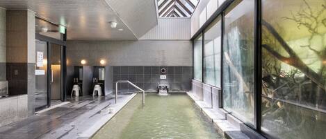 A modern indoor pool with clear glass walls, a tiled floor, and a visible water feature.