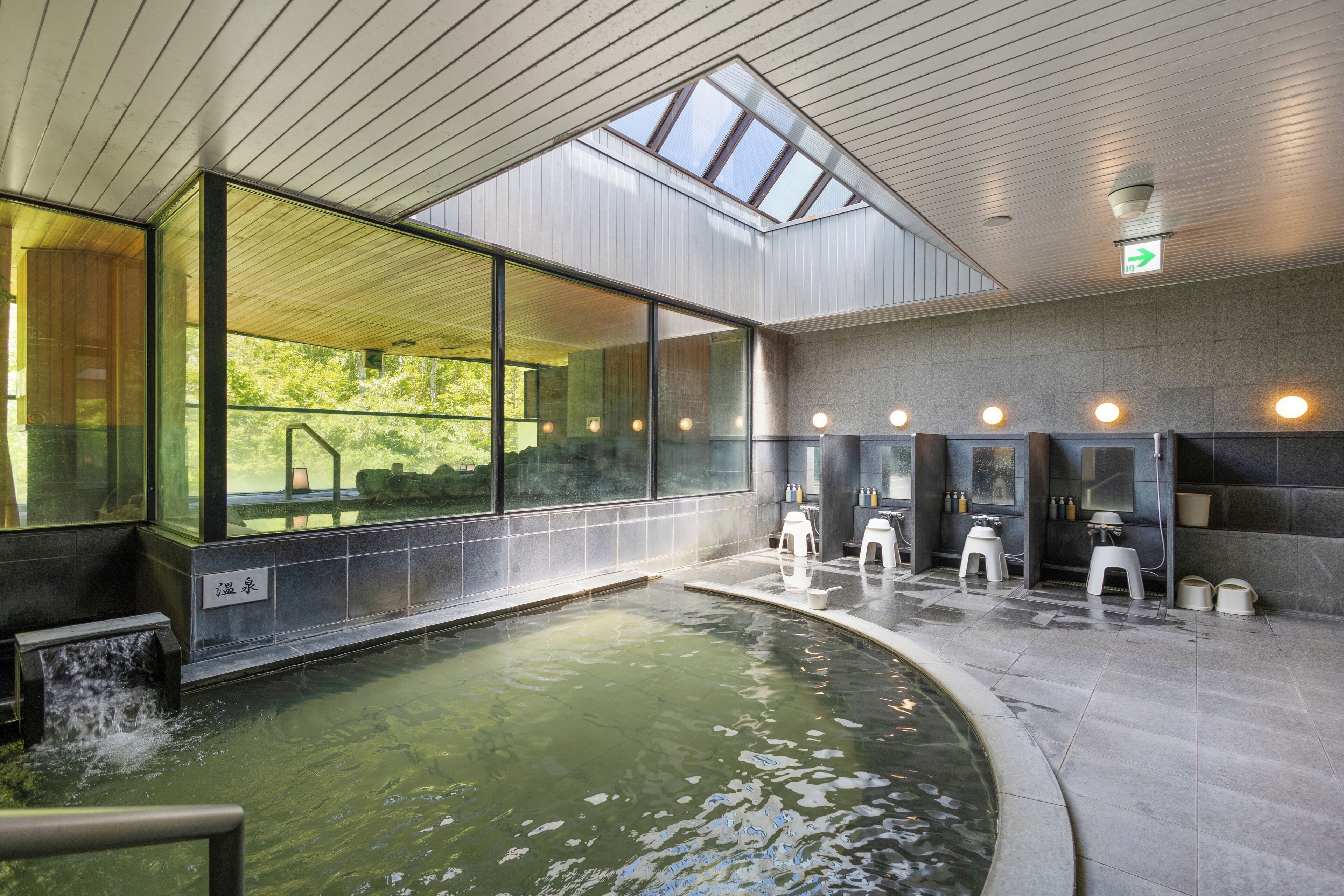 A modern indoor pool with clear glass walls, a skylight, and a stone floor.