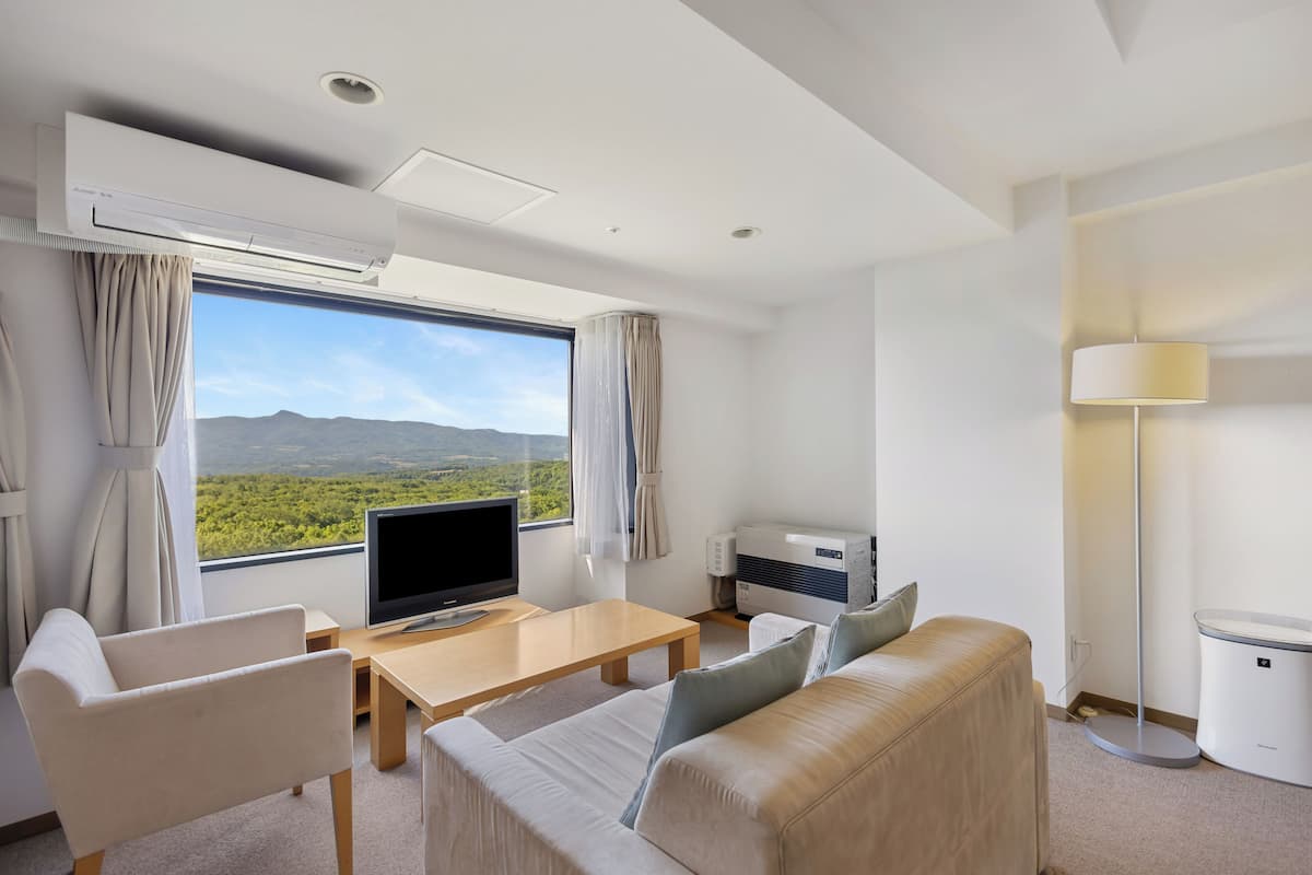 Ein modernes Hotelzimmer mit großem Fenster, einem Flachbildfernseher, einer Sitzecke, einem Couchtisch und einer Klimaanlage.