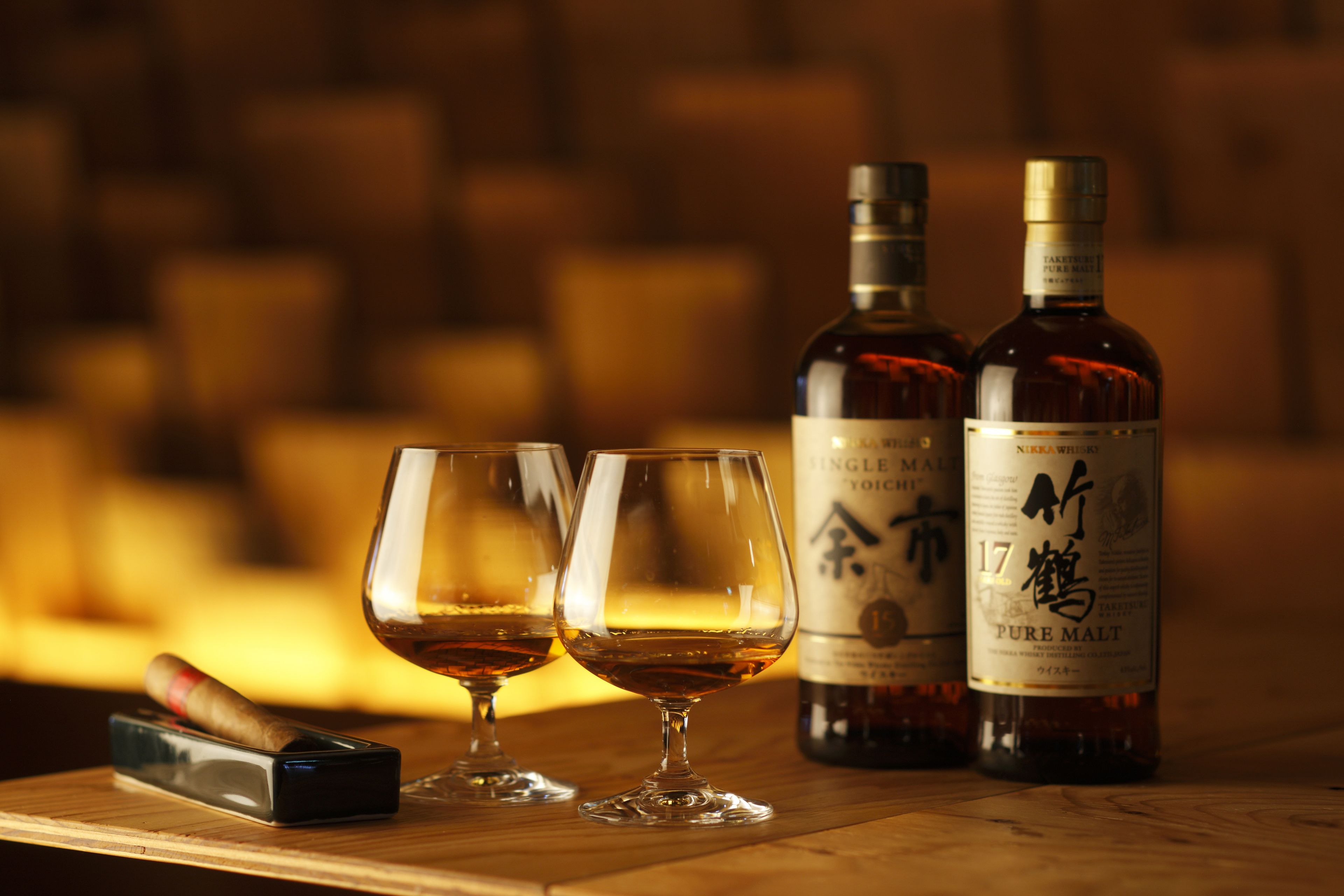 Two glasses of whiskey and two bottles of whiskey on a wooden table.