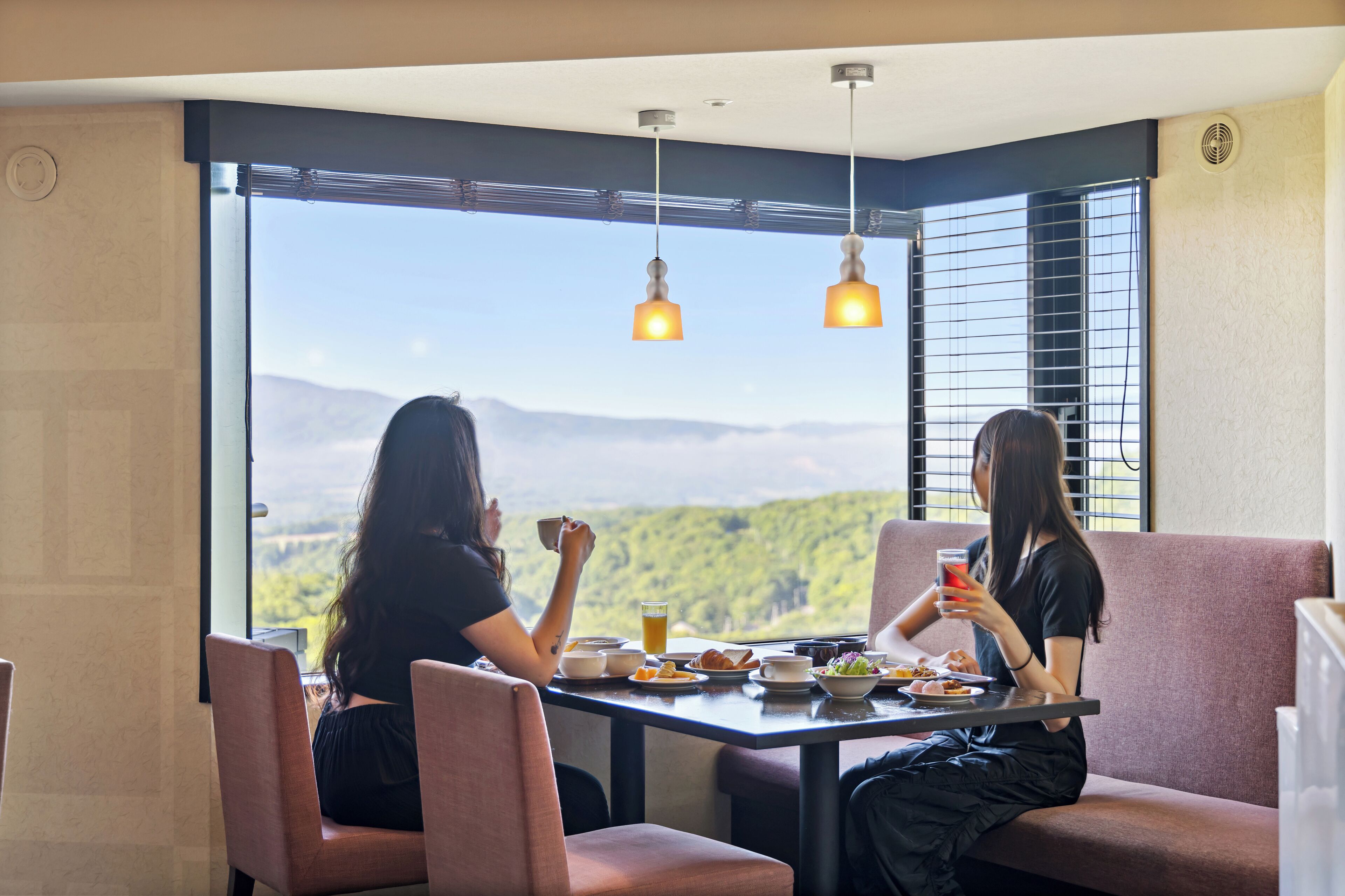 Two people dining at a table with a mountain view, two pendant lights, and a window with blinds.
