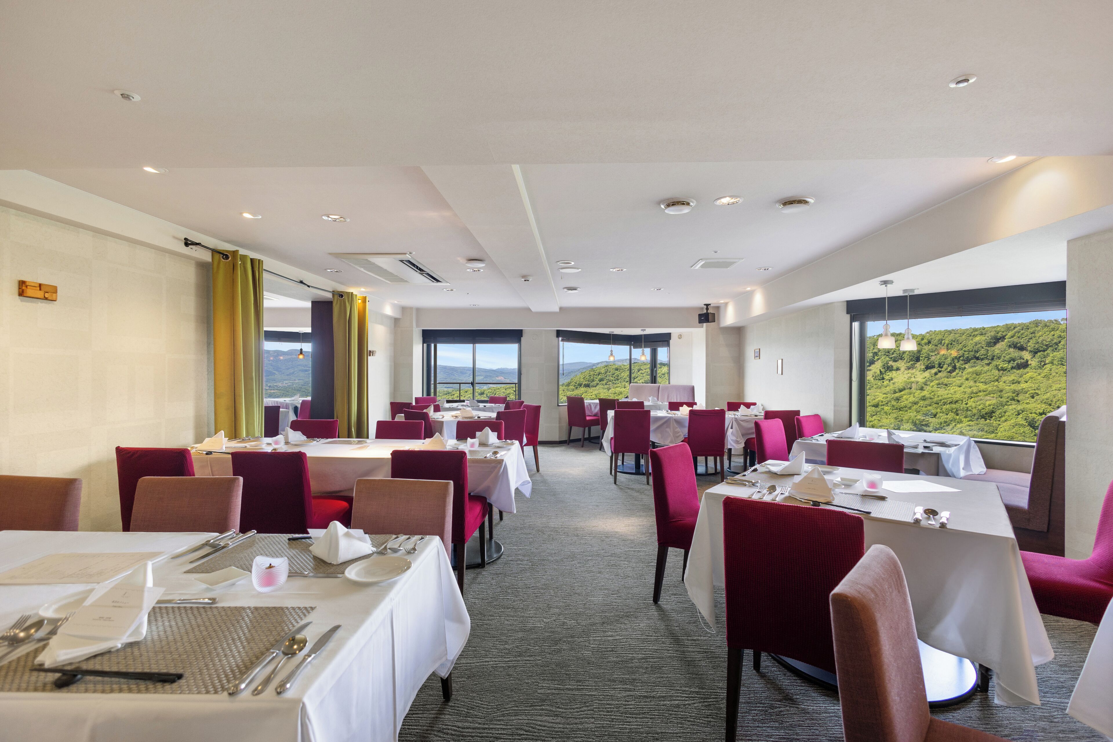 A restaurant with tables set for dining, large windows offering a view of greenery, and a modern interior design.