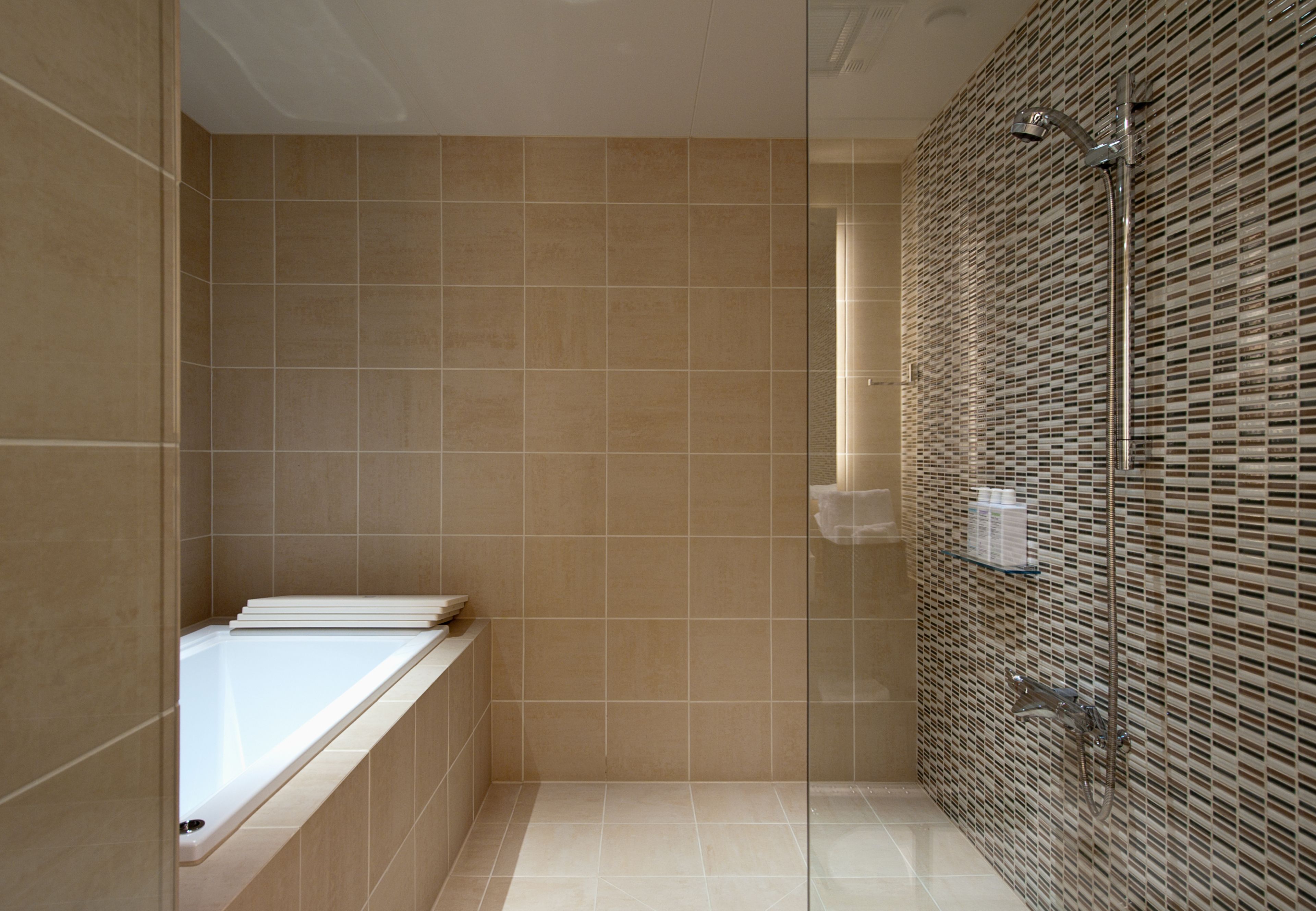 A modern bathroom with a bathtub, a glass shower enclosure, and tiled walls.