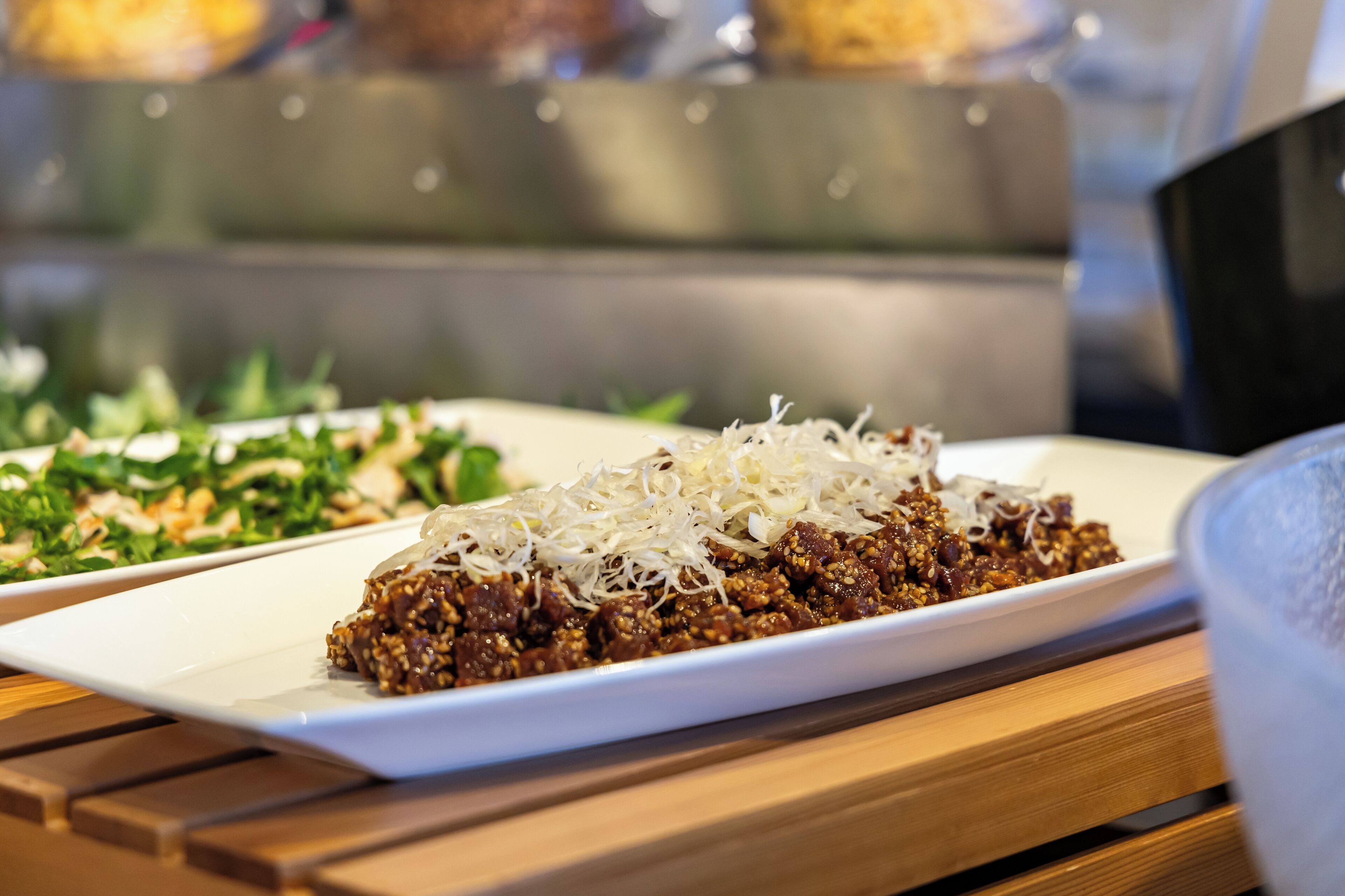 A white rectangular plate with a dish topped with shredded cheese and a side salad on a wooden table.