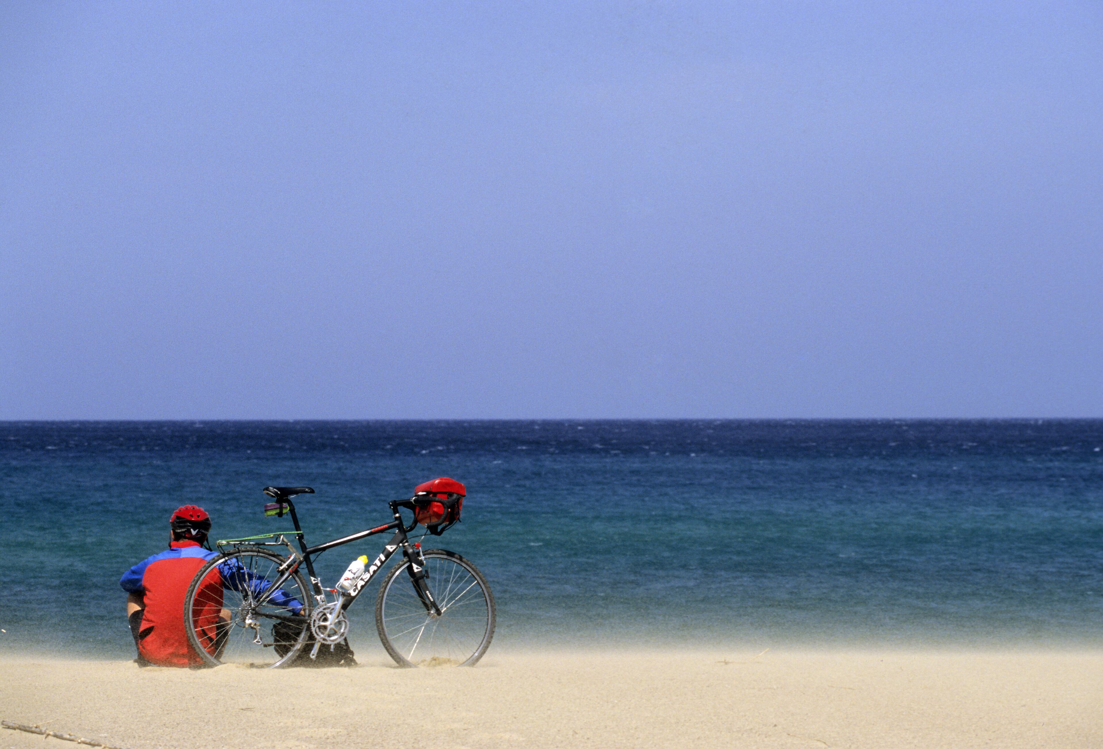 A beach scene with a bicycle and a person in red attire.