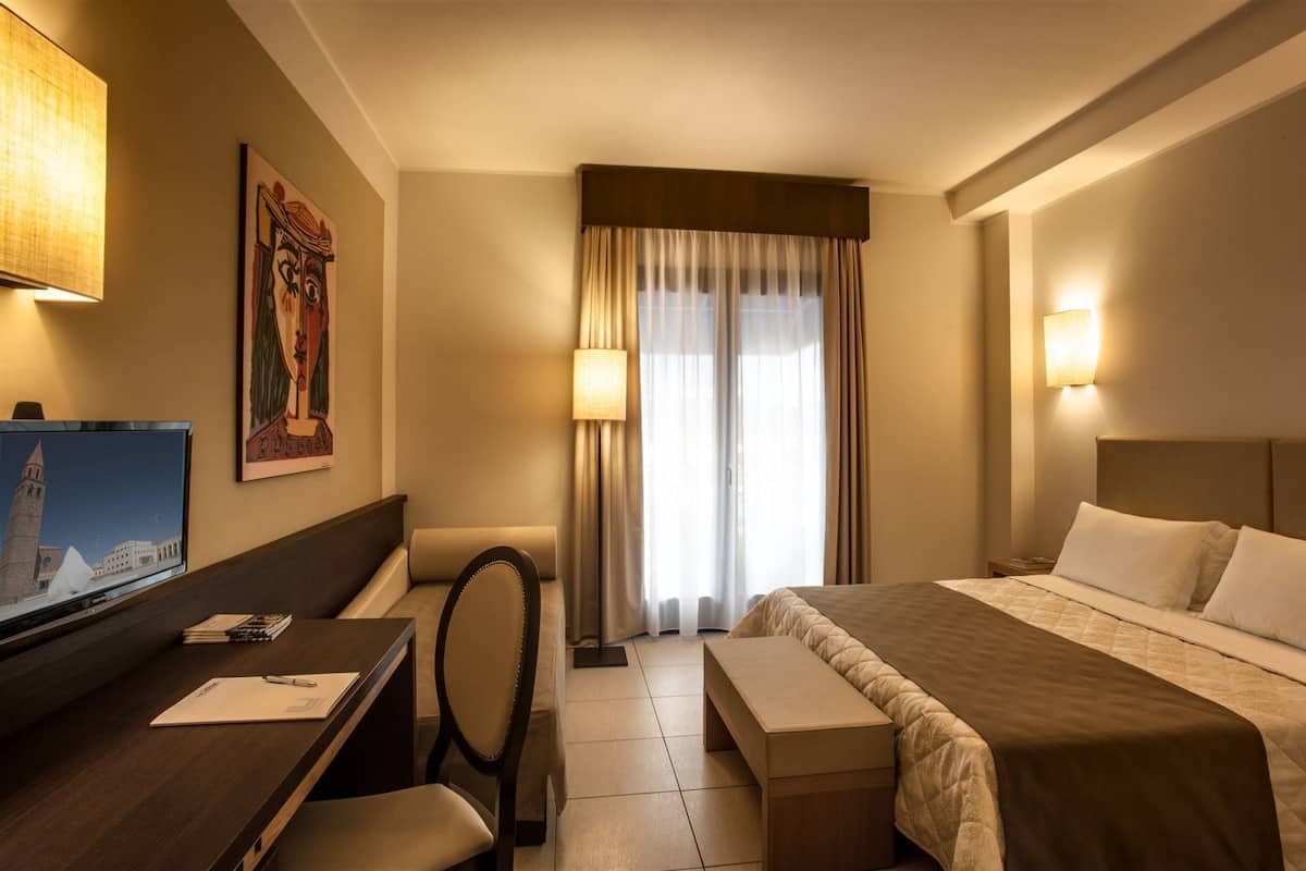 A hotel room with a bed, desk, chair, and a television displaying a cityscape.