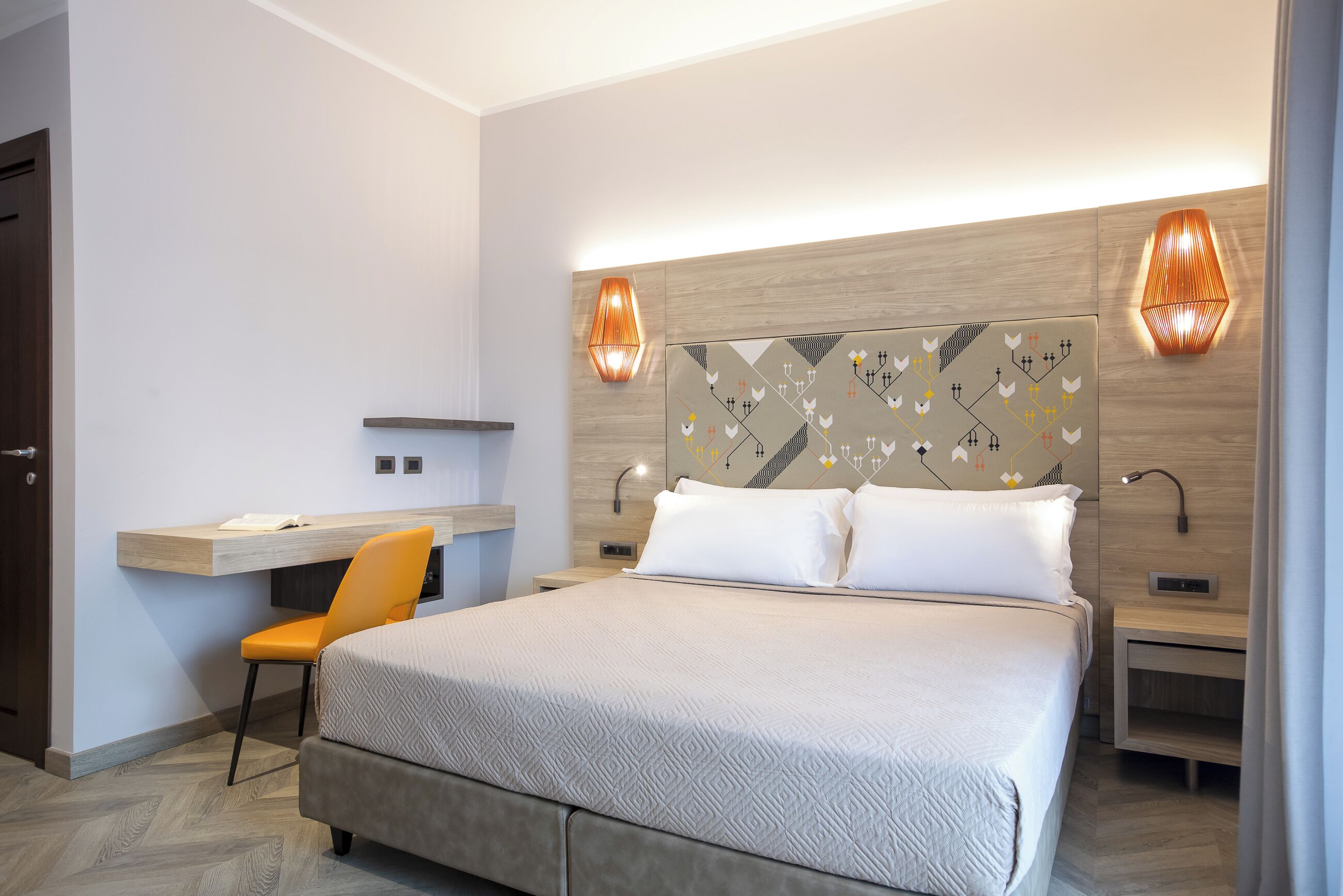 Ein modernes Hotelzimmer mit einem großen Bett, einem Schreibtisch und zwei Wandleuchten.