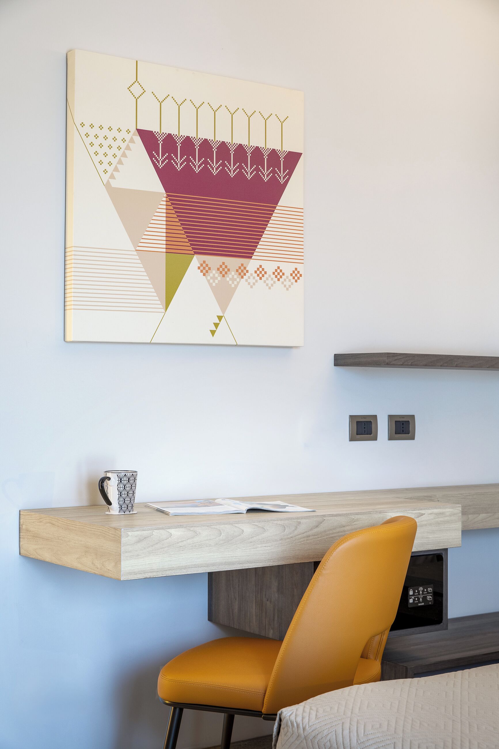 A modern room with a wooden desk, a yellow chair, and a geometric artwork on the wall.