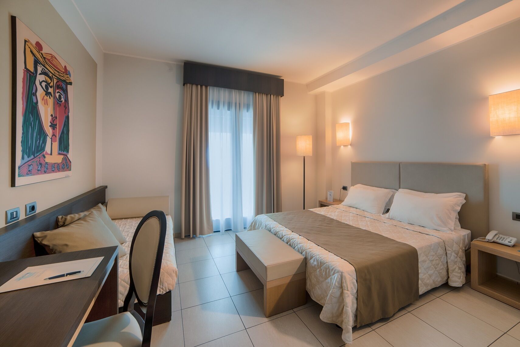 Una habitación de hotel con cama, escritorio, silla y un cuadro en la pared.