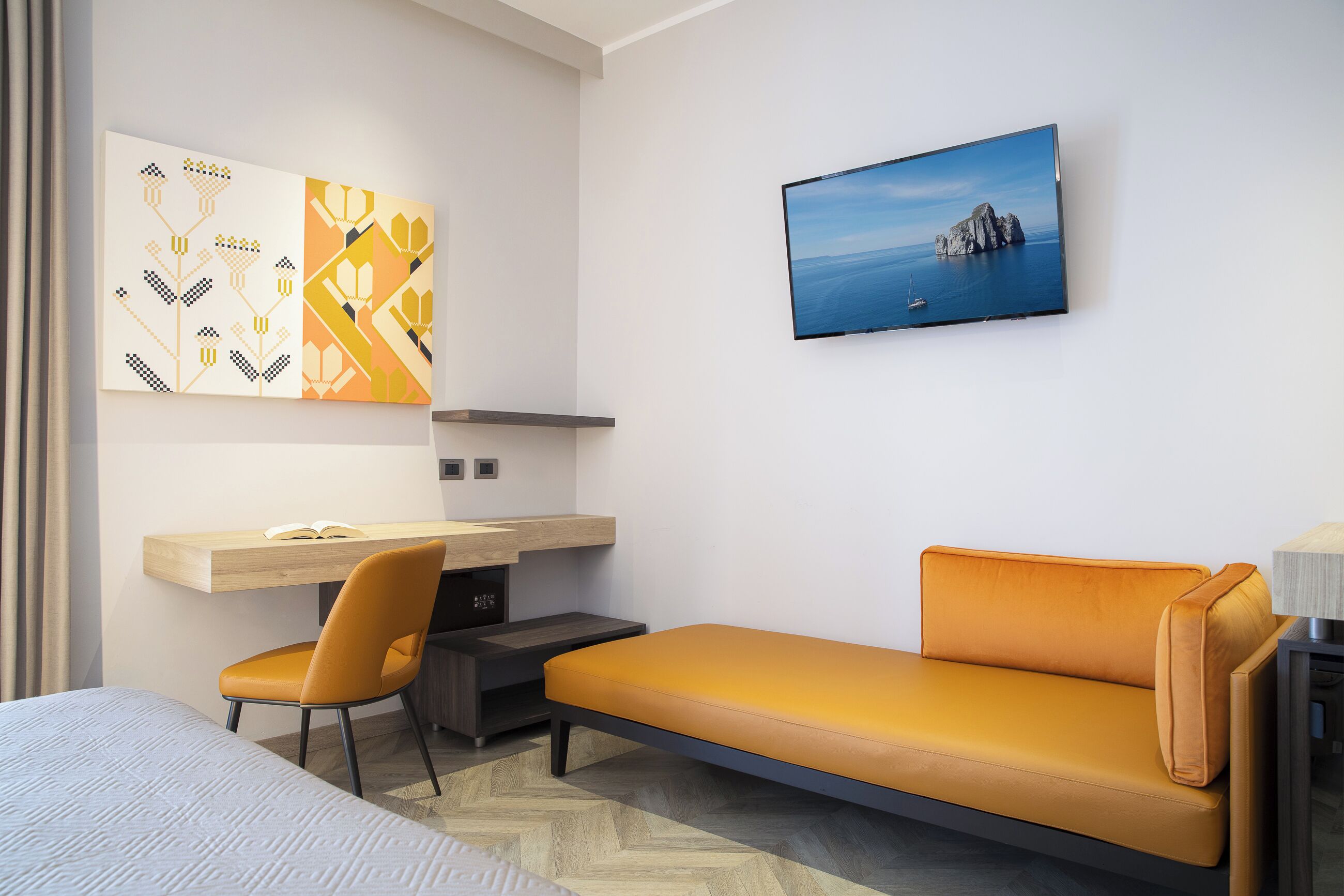 A modern hotel room with a bed, a sofa, a desk, and a TV.