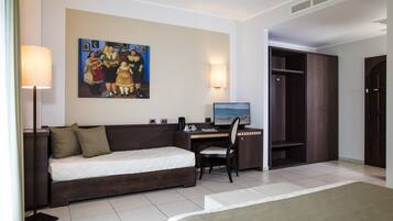 A hotel room with a bed, a desk with a computer, a chair, a wardrobe, and a painting on the wall.