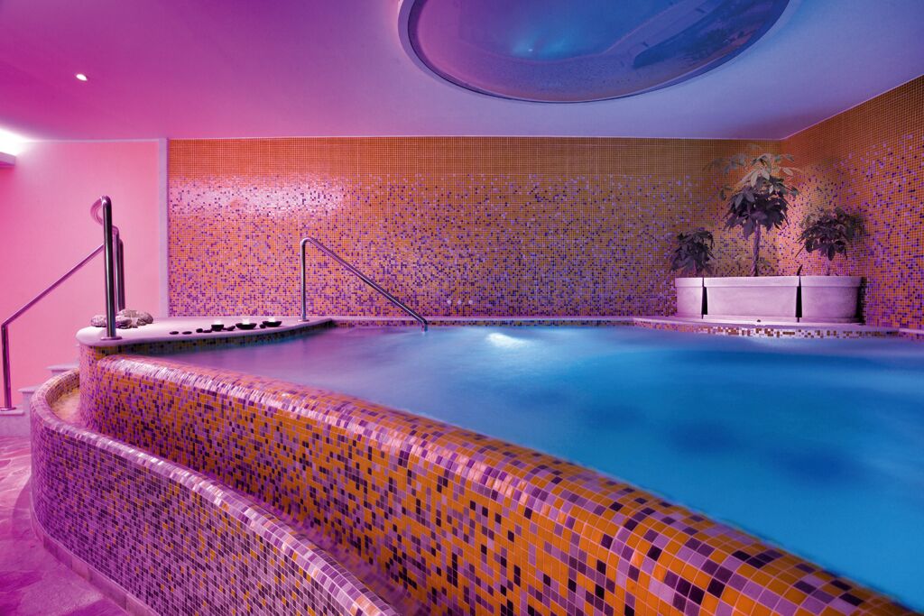A large indoor swimming pool with a tiled wall and steps leading into the water.