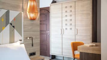 Habitación de hotel moderna con un armario de madera, una mesita de noche, una silla naranja y una lámpara fijada a la pared.