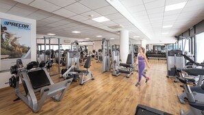 A gym with various exercise machines, a wooden floor, and a large mirror on the wall. - Lu' Hotel Carbonia (Carbonia)