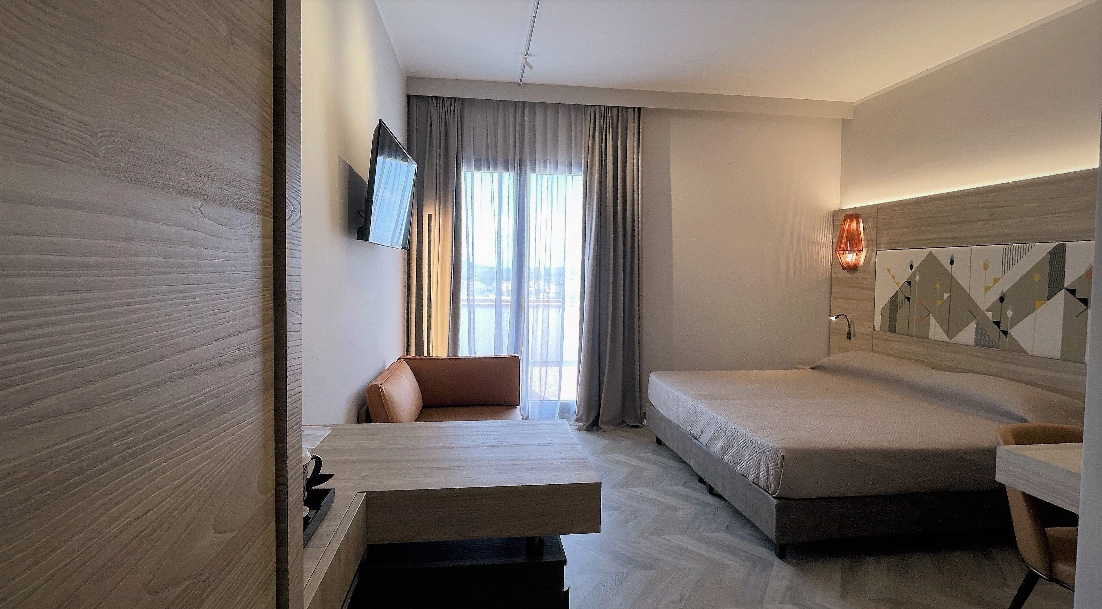 A modern hotel room with a bed, a desk, a chair, and a TV.