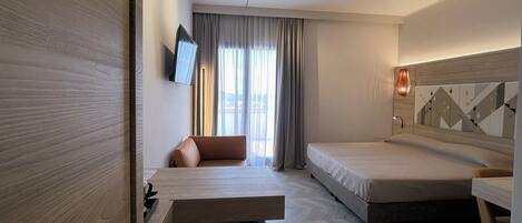 A modern hotel room with a bed, a desk, a chair, and a TV.