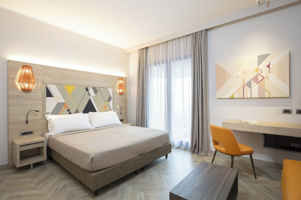 A modern hotel room with a large bed, a desk, and a chair.