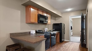 A kitchen with wooden cabinets, a microwave, a stove, a refrigerator, and a toaster. - Eagle's Den Suites Carrizo Springs a Travelodge by Wyndham (Carrizo Springs)