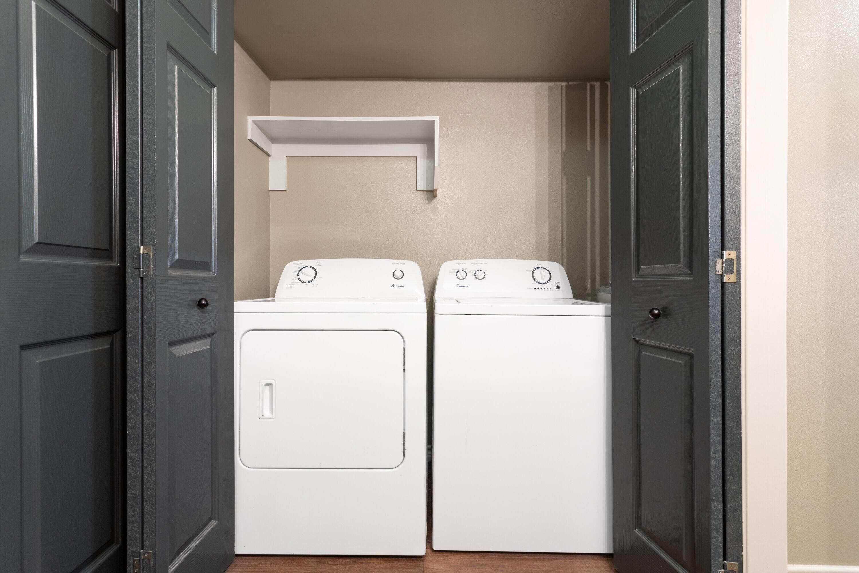 Une buanderie équipée de deux machines à laver à chargement frontal blanches, avec une étagère blanche placée au-dessus.