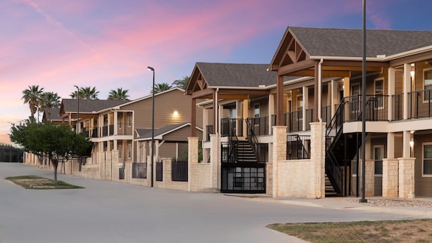 A multi-story hotel with balconies, a covered entrance, and a gated driveway. - Eagle's Den Suites Carrizo Springs a Travelodge by Wyndham (Carrizo Springs)