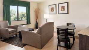 Habitación de hotel con sofá, sillas, una mesa de comedor, lámpara y cuadros en la pared.