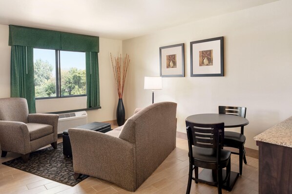 Habitación de hotel con sofá, sillas, una mesa de comedor, lámpara y cuadros en la pared.