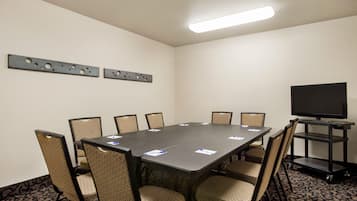 A conference room with a rectangular table, six chairs, a flat-screen TV on a stand, and a ceiling light fixture.