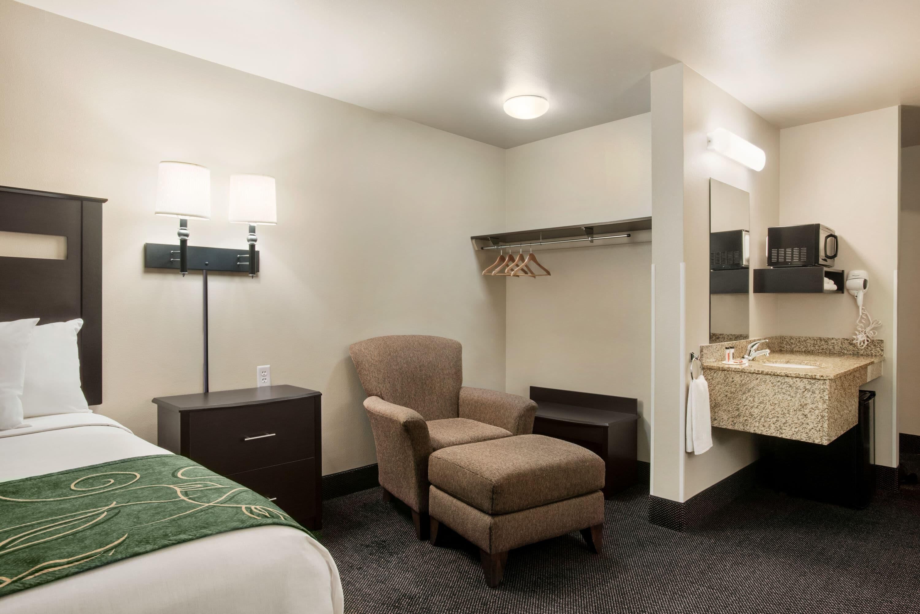 Une chambre d’hôtel comprenant un lit, une chaise, un bureau, une commode, un miroir, un lavabo et un porte-serviettes.