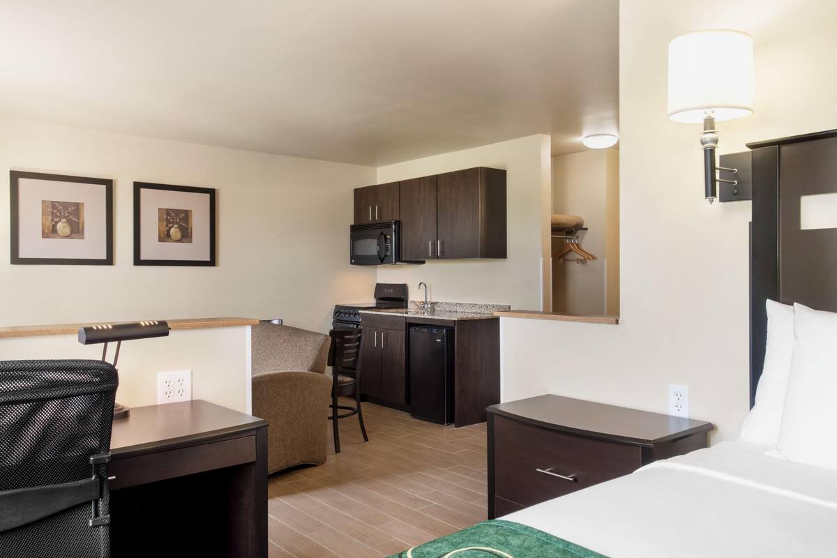 A compact hotel room with a kitchenette, a bed, a desk, and a chair.