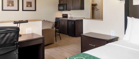 A compact hotel room with a kitchenette, a bed, a desk, and a chair.