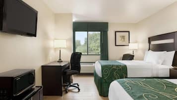 A hotel room with a TV, desk, chair, two beds, and a window.