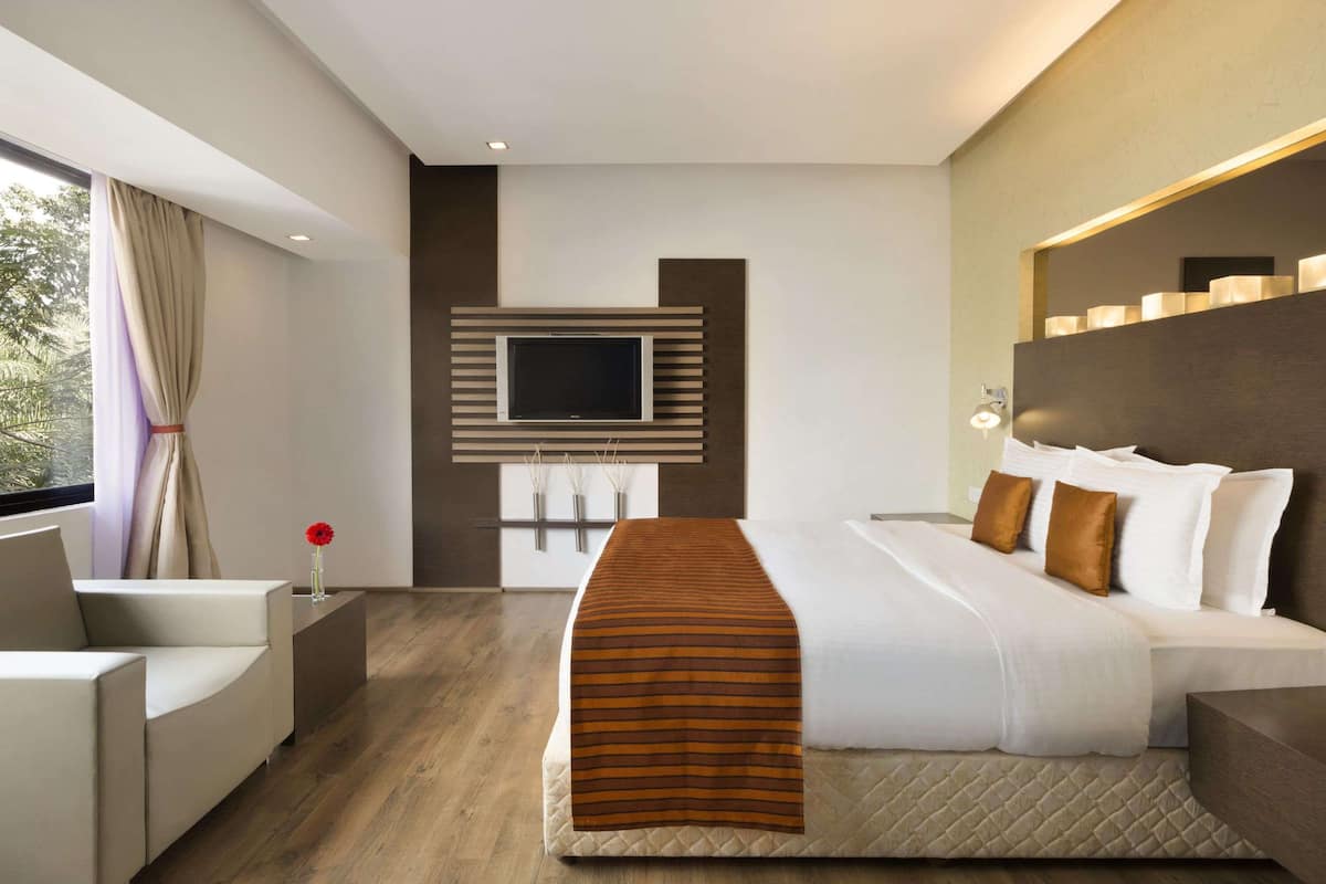 A modern hotel room with a large bed, a flat-screen TV mounted on the wall, a bedside table, and a window with curtains.