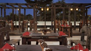 An outdoor dining area with wooden tables and benches, red napkins, and a wooden sculpture centerpiece.