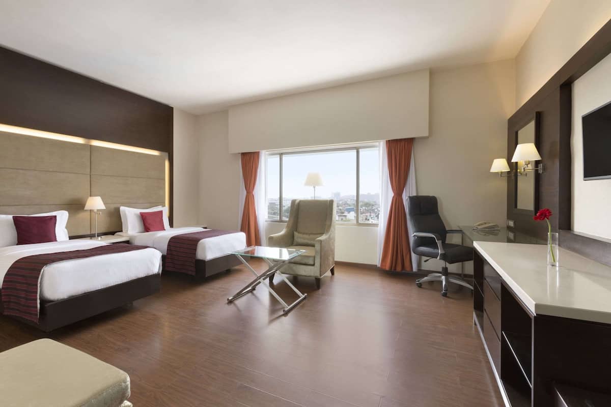 A hotel room with two beds, a desk, a chair, a TV, and a window with curtains.