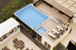A rooftop pool with a small adjacent hot tub, outdoor seating, and a staircase leading to an upper level.