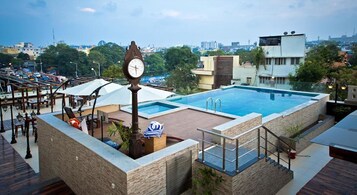 Una piscina en la azotea con un reloj, sillas de descanso y vistas de la ciudad.