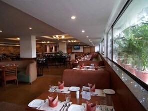 A restaurant with booths and tables, a brick wall, and a large window with a view of greenery.