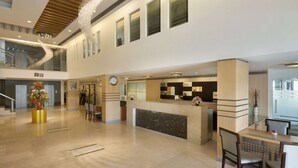 A spacious lobby with a reception desk, a clock, and a staircase leading to an upper level.