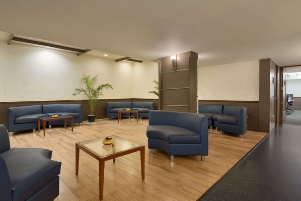 A modern lobby with blue sofas, a glass coffee table, and a wooden floor.