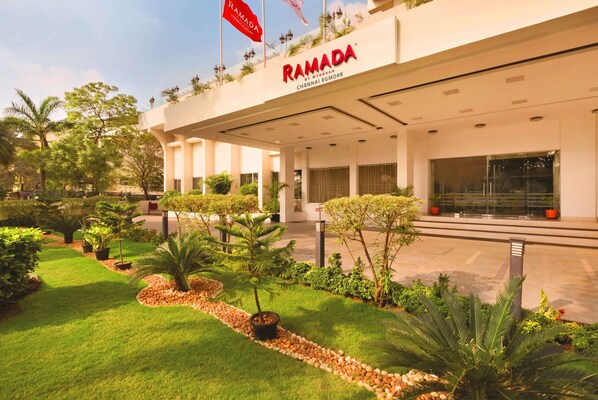 A modern hotel entrance with a well-maintained garden and a clear view of the building's name.